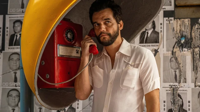 El actor brasileño Wagner Moura, caracterizado como Marcelo, su personaje en O Agente Secreto, auricular en la oreja en una cabina telefónica en una escena de la película.