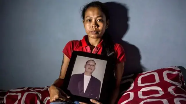 इंडोनेशिया की एक महिला अपने पति की तस्वीर के साथ, जिनकी मौत अवैध शराब पीने से हुई थी.