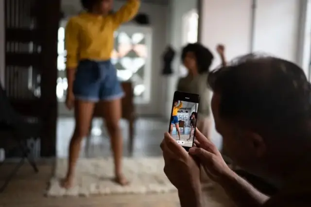 Um pai filmando duas crianças dançando
