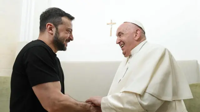 Ukranian President Volodymyr Zelensky and Pope Francis shake hands and smile 