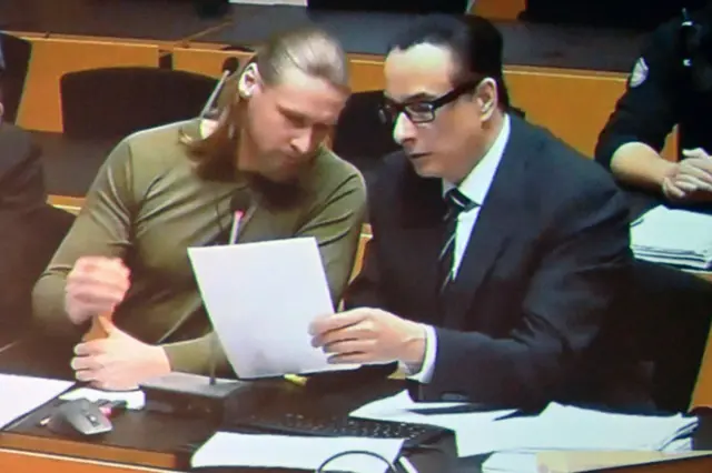 Мужчина с длинными волосами, зачесанными назад хвостом, и мужчина в костюме смотрят документы в суде