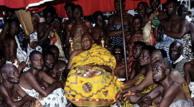 The Asantehene, wearing yellow robes, sitting with his court