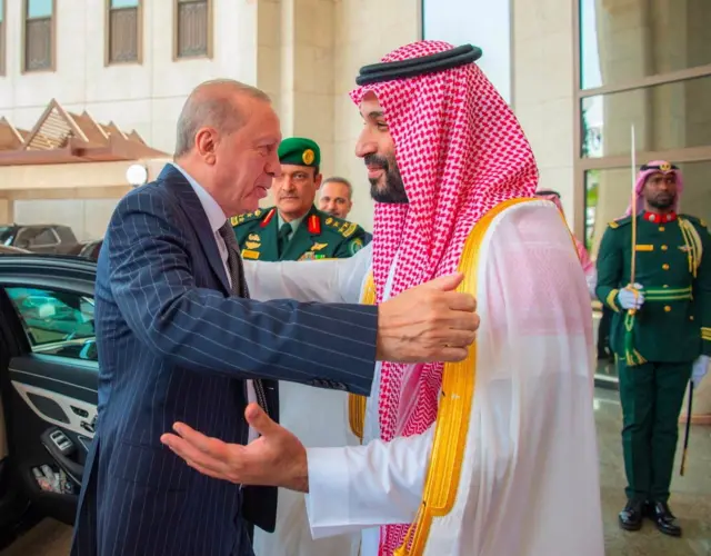 Erdogan, con un traje azul a rayas, abraza al príncipe Bin Salman, quien viste una túnica blanca con una ghutra roja. 