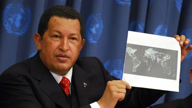Уго Чавес у темному костюмі та червоній краватці на тлі синього полотна із символікою ООН демонструє чорно-білу карту світу, роздруковану на аркуші паперу А4