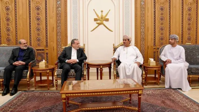 豪勢なじゅうたんの敷かれた室内に椅子が横並びに置かれ、スーツ姿のアラグチ氏と、白い長衣を来たブサイディ氏が座って話している。それぞれの両側にも関係者が座っている