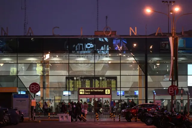 Personas caminan frente a la entrada del viejo aeropuerto Jorge Chávez de Lima en una imagen nocturna. 