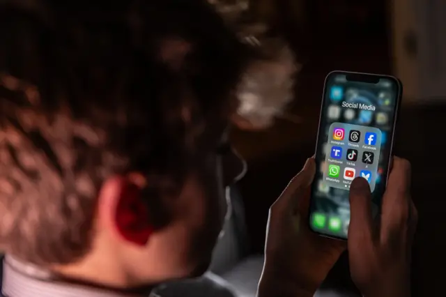 طفل يستخدم هاتفاً يظهر عليه بعض من منصات التواصل الاجتماعي