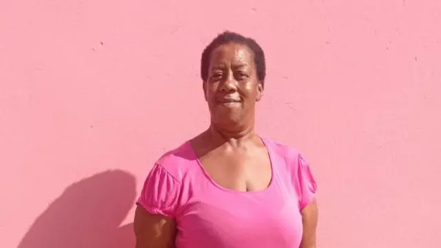 Miranda Beazer, usando uma blusa rosa diante de um fundo cor-de-rosa