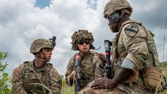 迷彩服を着て銃器を手にした兵士3人が草むらで集まっている