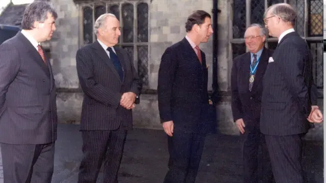 Cuatro hombres con traje de pie frente a una casa señorial.