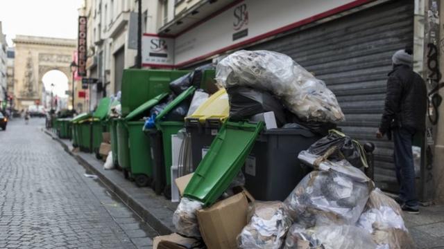 Un hombre camina junto a contenedores llenos de basura.