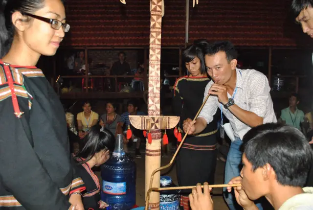 Hình tác giả bài viết (mặc áo carô) uống rượu cần trong buổi xem cồng chiêng