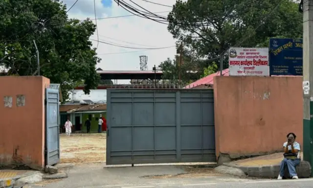 डिल्लीबजार कारागारको कार्यालय। कार्यालयको गेटभित्र केही टहरा र मानिसहरू र छेउमा नेपाल प्रहरीको एउटा चौकीको बोर्ड देख्न सकिन्छ