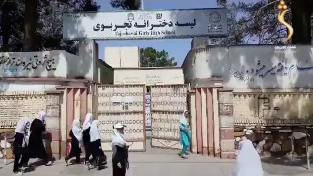 Afghan girls walk near the entrance of a school in the city of Herat, Afghanistan.