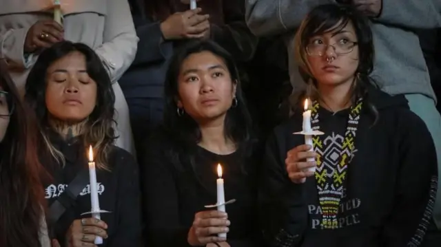 Tres personas sostienen velas en una de las vigilias por las víctimas del atropello en Vancouver