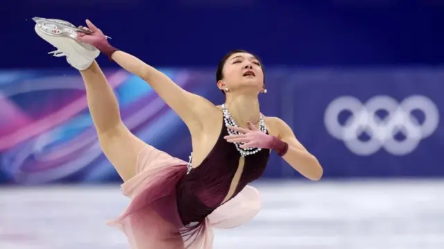 えんじと白の衣装の坂本が右手で、高く上げた左足のスケート靴の刃をつかんでいる