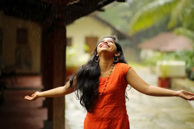 Young woman in traditional wear getting drenched by rain.
