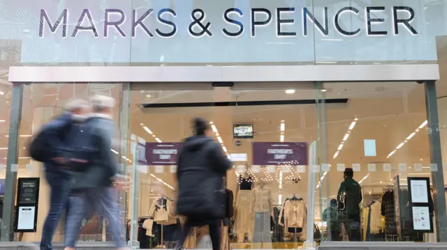 Fachada de una tienda de Marks & Spencer, con personas de figura borrosa dirigéndose hacia la puerta para entrar