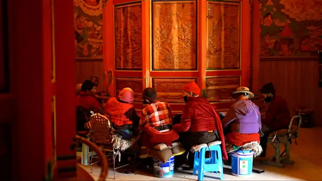 Mulheres tibetanas sentadas em volta de uma roda de oração em um monastério