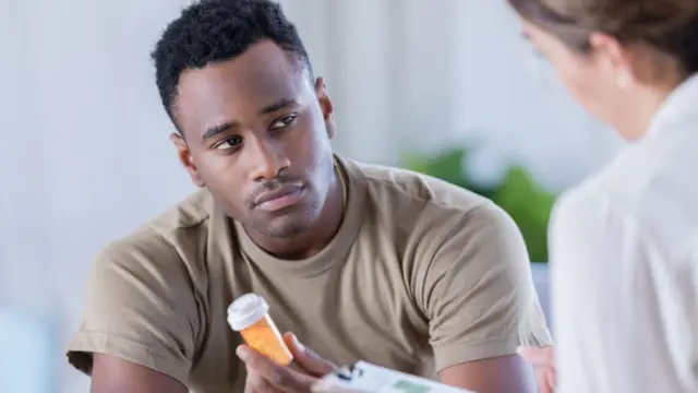 Un hombre sostiene un frasco de píldoras mientras mira con preocupación a una doctora