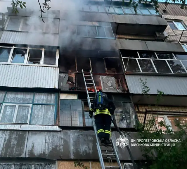 пожежник по драбині лізе у будинок, який димить 
