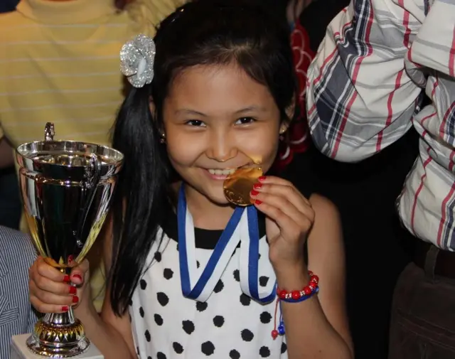 Кичкина Бибисора бир қўлида кубок, иккинчи қўлидаги олтин медални тишлааб турипти