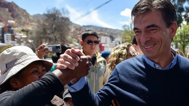 Rodrigo Paz sonríe mientras sostiene la mano de una mujer que lo mira con entusiasmo.