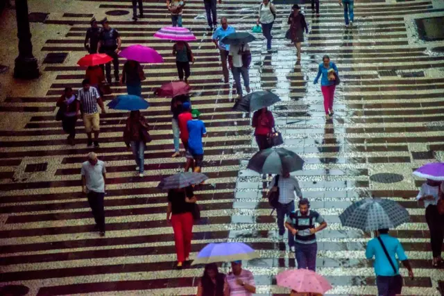 Pessoas caminhandoapostas esportivas on linecalçadaapostas esportivas on linedia chuvoso; algumas carregam guarda-chuva