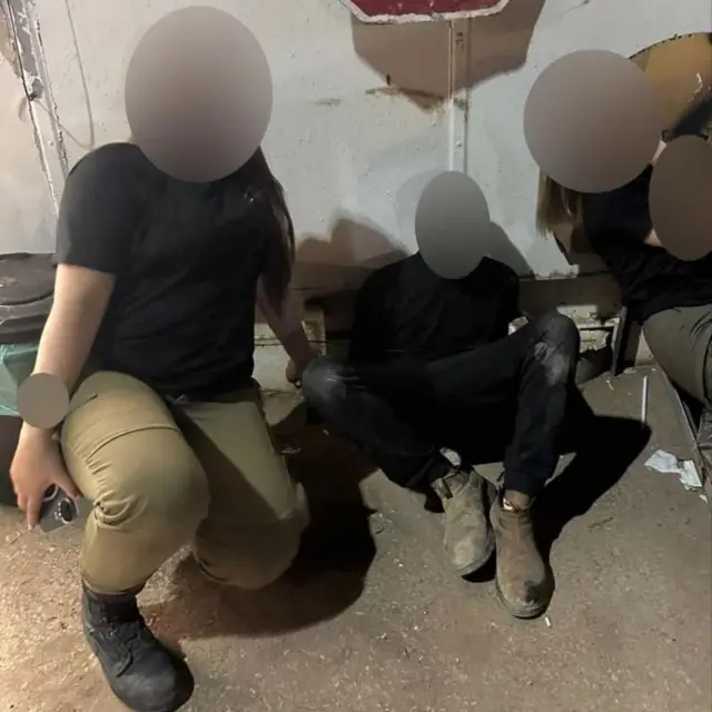 Foto de um homem e um jovem em um quarto, um deles com roupas militares. Os rostos estão borrados.