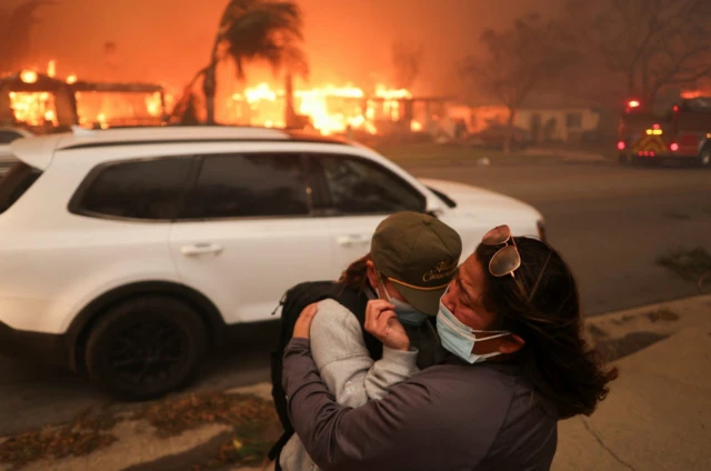 Duas pessoas se abraçam enquanto evacuam após fortes ventos que alimentam incêndios florestais devastadores na áreagood online casinoLos Angeles