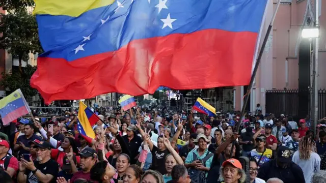 黄・青・赤に白い星が半円を描くヴェネズエラ国旗を持った大勢の男女が通りを行進している