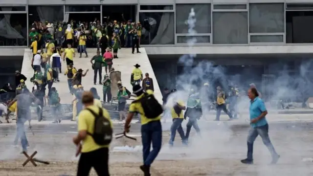 Pessoas com camisetas amarelas atirando objetosgrupo do luva betdireção à rampa do Palácio do Planalto 