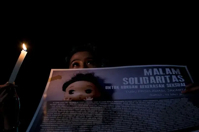 Seorang gadis kecil memegang lilin dengan poster solidaritas untuk korban kekerasan seksual.