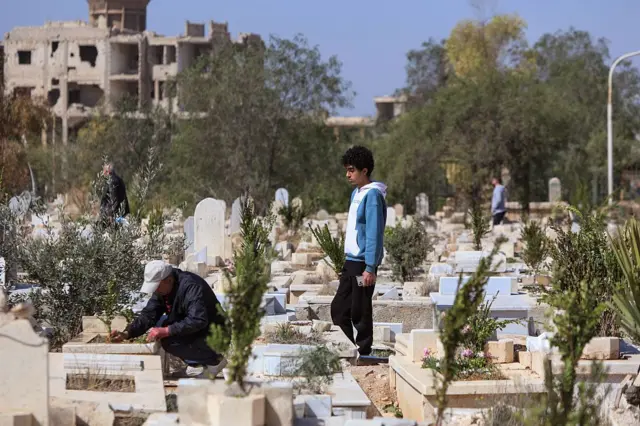 يزور الناس قبور أقاربهم كما جرت العادة في اليوم الأول من عيد الفطر - المقبرة المتضررة في مخيم اليرموك للاجئين الفلسطينيين في دمشق.