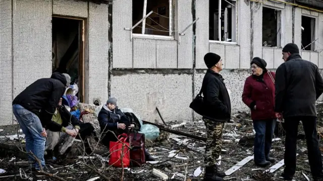 கிழக்கு யுக்ரேன் நகரமான சுகுவேயில் குண்டுவெடிப்புகளுக்குப் பிறகு மக்கள் ஓர் அழிக்கப்பட்ட கட்டிடத்திற்கு வெளியே நிற்கிறார்கள்