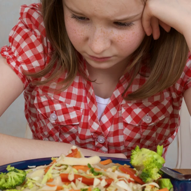 Niña con expresión triste frente a un plato de comida