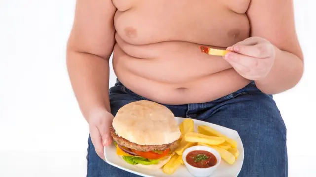 Garoto sem camisa comendo um hamburger e batatas fritas