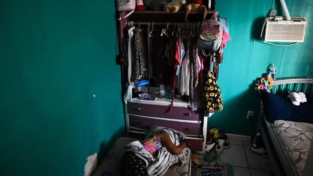 Criança repousa no quarto, onde um aparelho de ar-condicionado permanece desligado na parede