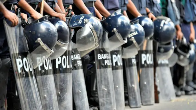 পুলিশ সদস্যরা তাাদের হেলমেট ও শিল্ড নিয়ে দাঁড়িয়ে আছেন