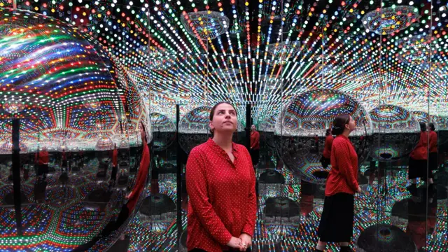 Um visitante em uma das “Infinity Rooms” de Kusama, visto refletido várias vezes nos espelhos cercados por luzes