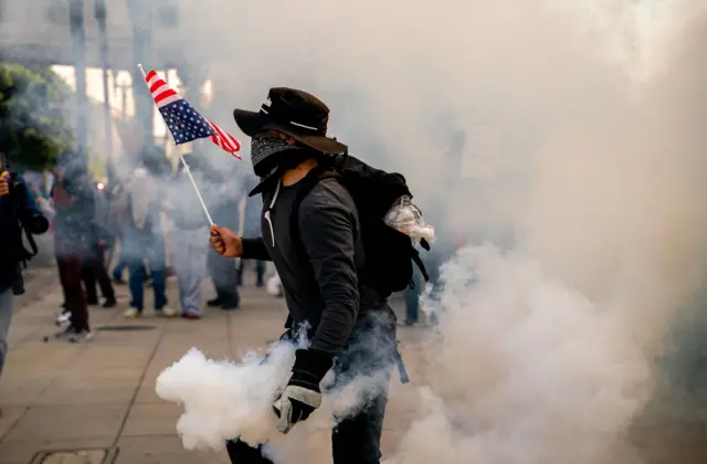 Muškarac u dimu suzavca drži američku zastavu