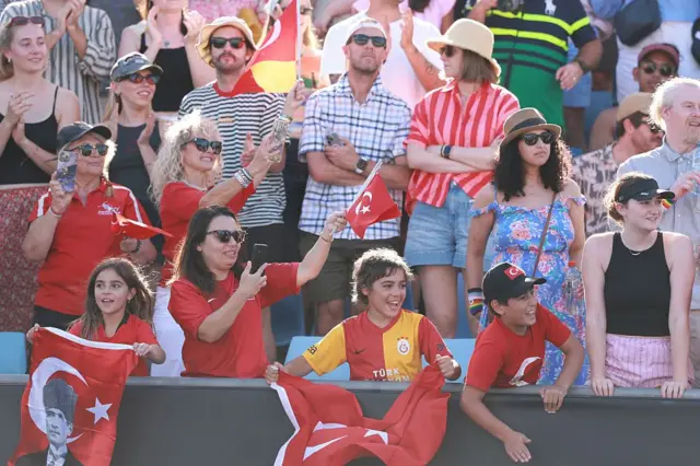 Türk bayraklı çocuklar ve kadınlardan oluşan bir grubu tribünlerde görüyoruz. Baktıkları yerde Zeynep Sönmez'in olduğu anlaşılıyor.