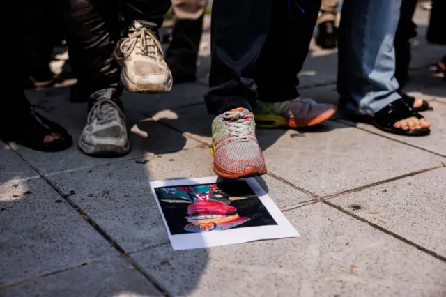 म्यांमार के सैन्य शासकों के फोटो पर पैर रखकर विरोध जताते लोग