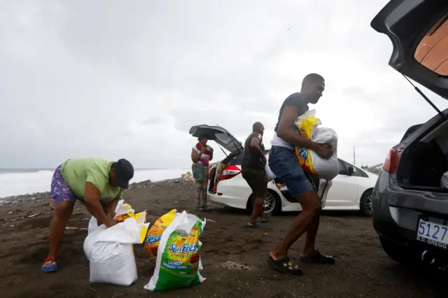 Varias personas cargan costales de arena a sus vehículos en una playa de Jamaica