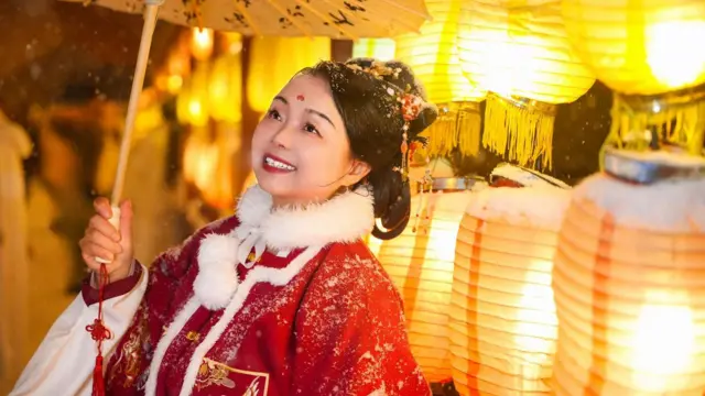 Su Min aparece vestindo um traje tradicional chinês. Ela estácassino skrillpé, usando um vestido vermelho com golacassino skrillpele na frentecassino skrillvárias lâmpadascassino skrillpapel amarelas acesas.