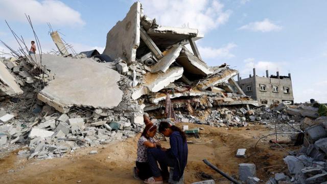 فتيات يجلسن أمام مبان مدمرة في غزة.
