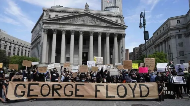 متظاهرون يقفون خلف لافتة ضخمة مكتوب عليها جورج فلويد