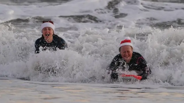 Women wearing Santa hats bodyboard on Christmas Day at Tynemouth Beach on the North East coast.