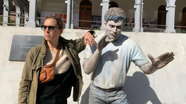 Paige Nichols, uma jovem brancaf12 bet pagaóculos escuros, ao ladof12 bet pagauma estátua