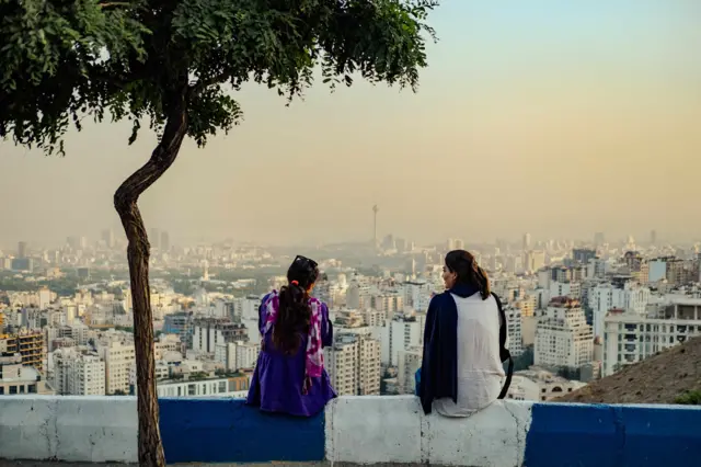 Mulheres iranianas sem o hijab obrigatório sentam-se em Bam-e Tehran (Telhado de Teerã) com vista para a cidade de Teerã, 2024